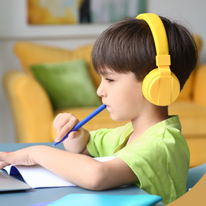 Young boy wearing yellow headphones studying on a laptop at home.