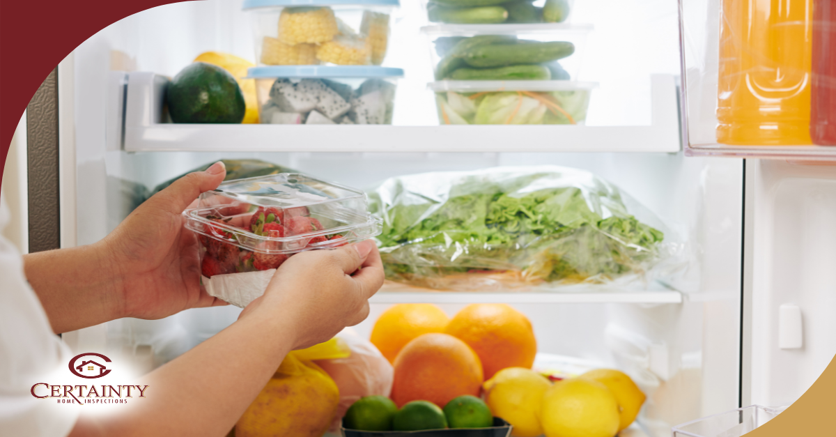 Person placing fresh strawberries in a refrigerator filled with fruits and vegetables.