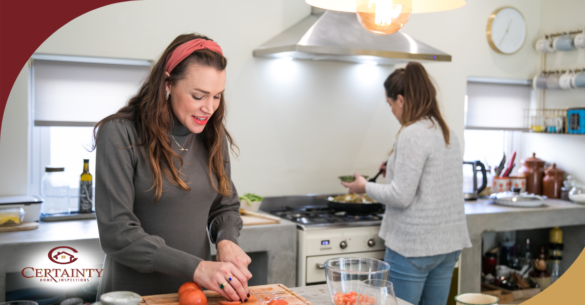 Two women preparing food together in a bright kitchen, one chopping vegetables and the other cooking on the stove.