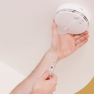 A person installing a smoke detector on the ceiling with a screwdriver, smiling