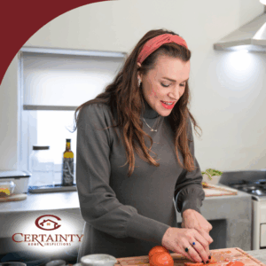 Two women preparing food together in a bright kitchen, one chopping vegetables and the other cooking on the stove.