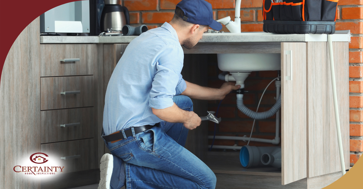 Plumber repairing pipes under a kitchen sink.