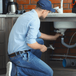 Plumber repairing pipes under a kitchen sink.