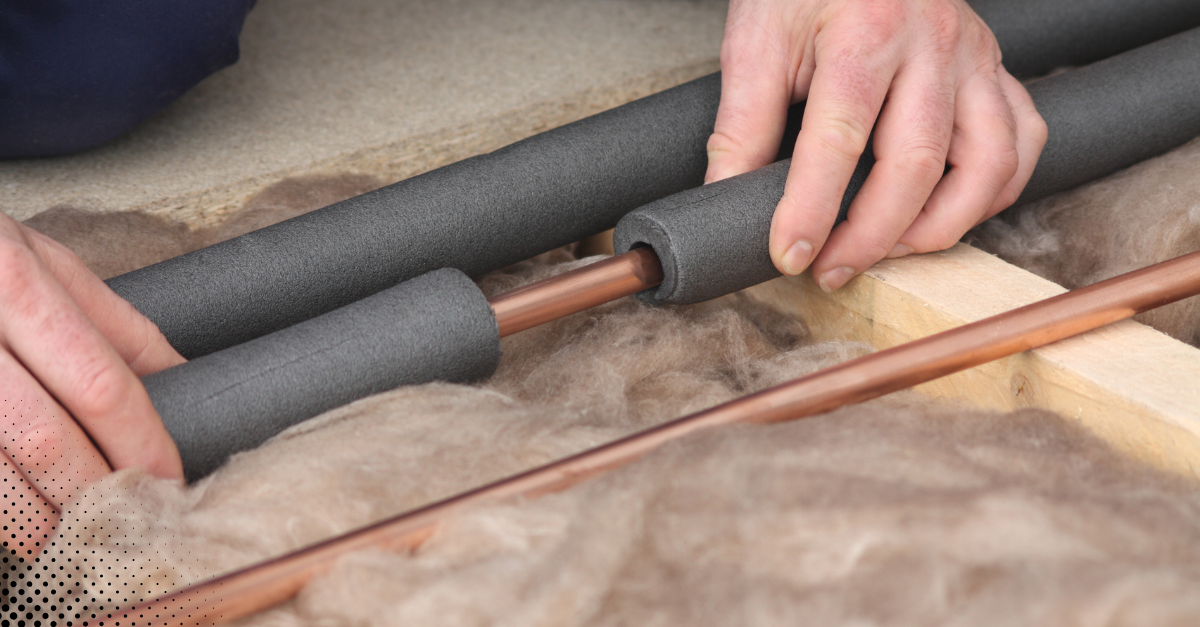 Hands installing foam insulation around copper pipes.