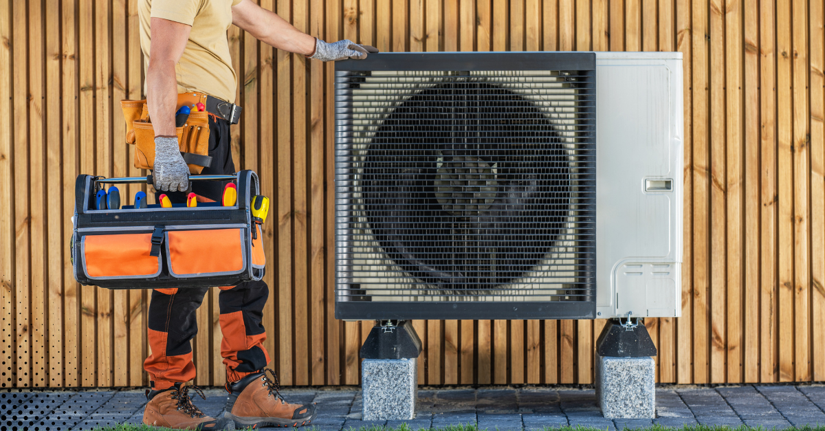 Technician holding a tool bag near a residential HVAC outdoor unit.